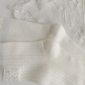Close-up of white ribbed knit crew socks featuring a delicate embroidered side patch
