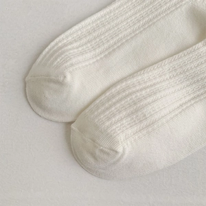 Macro detail of cream knit cotton socks showing delicate vertical rib texture and stitching
