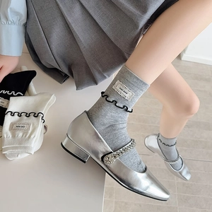 Détail de chaussettes grises à bord volanté noir et chaussures Mary Jane argentées