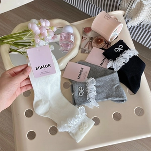 Detail of knit socks featuring lace trim and a decorative pearl bow in a soft setting