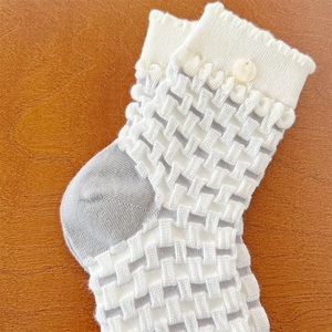 Detail view of white knitted crew socks with embossed check texture and ruffled button cuff
