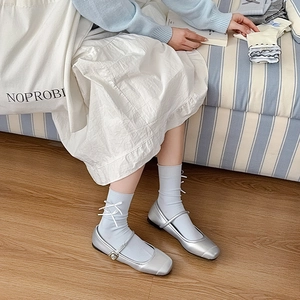 Close-up of silver Mary Jane flat shoes paired with blue crew socks and white bows