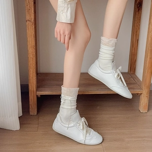 Dettaglio di sneaker bianche stringate con calze bianche su pavimento in legno naturale