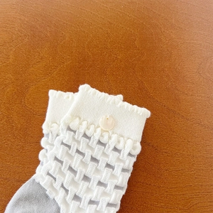 Detailed shot of hollow lattice knit baby socks with scalloped edges and shell button
