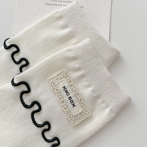 Détail de chaussette en coton blanc avec bord ondulé noir et étiquette en dentelle style