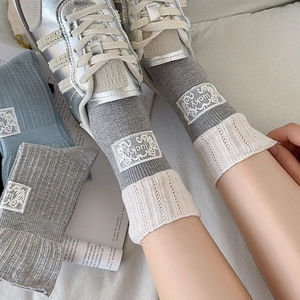 Detail of grey ribbed mid-calf socks featuring lace trim and a lucky embroidered patch