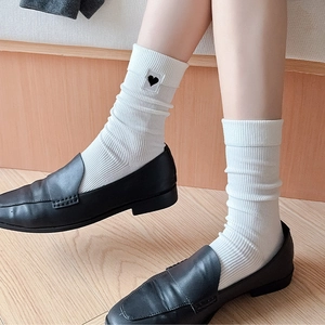 Detailed view of white ribbed socks with black heart embroidery and black leather loafers