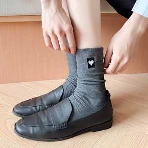 Close-up of gray ribbed crew socks with heart embroidery worn with black leather loafers