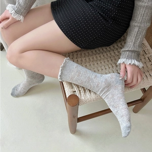 Detail of gray mid-calf socks with bow pattern and white lace trim for a cozy look