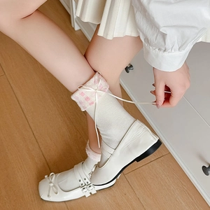 Détail de chaussettes blanches avec bord à carreaux roses et ruban nœud en soie élégant