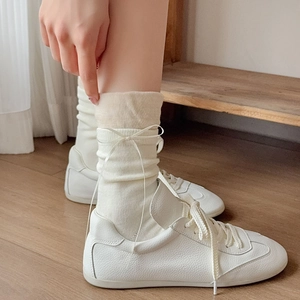 Dettaglio di calze bianco crema con fiocchi di nastro e sneakers in pelle bianca