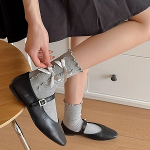 Detail of grey ribbed mid-calf socks featuring frilly edges and white satin bows