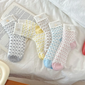 Detail of four-color mid-calf socks with lattice weave and decorative button on white cloth
