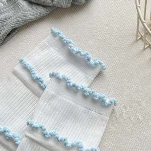 Détail de chaussettes en coton blanc avec bords volantés bleu clair et maille côtelée