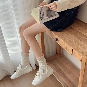 Dettaglio di calze in maglia crema con fiocco e scarpe da ginnastica bianche casual