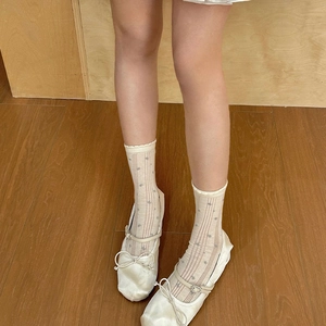 Elegant cream ballet flats with bow and polka dot knit socks on wooden floor