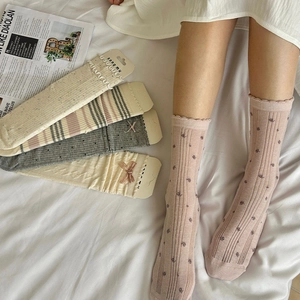 Détail de chaussettes à nœuds avec bords à volants en blanc crème, gris et motifs floraux