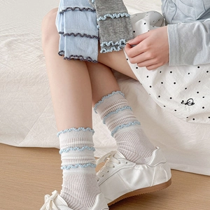 Détail de chaussettes à volants en bleu clair et gris portées avec des baskets blanches
