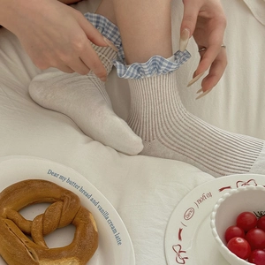 Off-white ribbed mid-calf socks with blue checkered ruffle trim in a cozy home setting