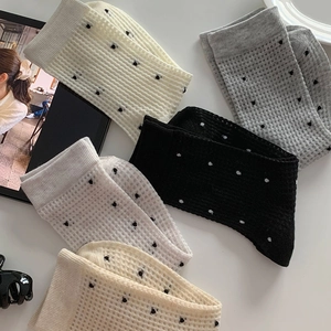 Detail of polka dot waffle knit mid-calf socks in white, beige, grey, and black tones