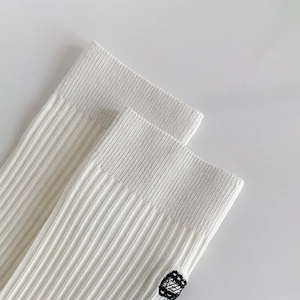 Close-up of white ballet style ribbed socks featuring a black embroidered logo detail