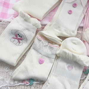 Dettaglio calze in maglia color crema con balze, fiocchi rosa e ricami di cuccioli
