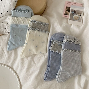 Vue détaillée de chaussettes à froufrous pour femmes en bleu et gris sur un lit blanc