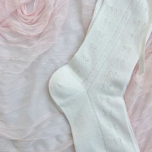 Close-up of white knitted crew socks featuring delicate bow patterns and rib texture