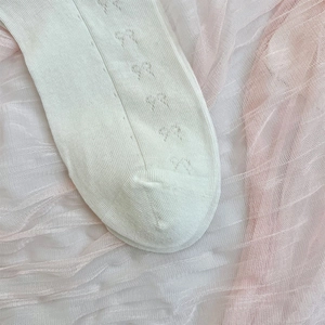 Detail of white mesh socks featuring delicate bow jacquard patterns and fine knit texture
