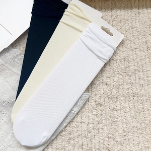Trois paires de chaussettes à côtes en blanc, beige et noir sur fond de dentelle texturée