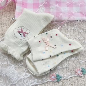 Dettaglio di due paia di calze bianco crema con fiocchi rosa e ricamo a cucciolo