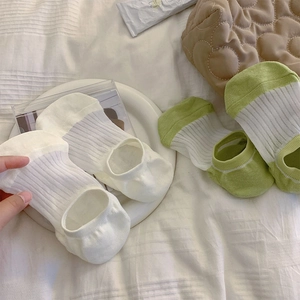 Dettaglio di calzini invisibili a righe bianche e verdi su un morbido letto di cotone