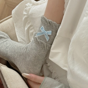 Close-up of light grey socks with ruffled edges and a blue plaid bow on white bedding