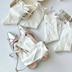 Detail of white pointelle knit socks with silk bow ties and silver Mary Jane shoes