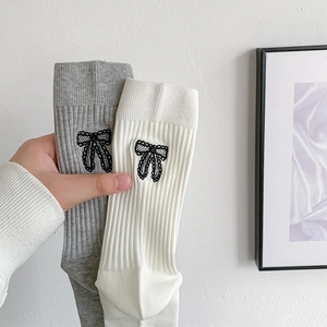 Detail of ballet style knit socks with black lace bows and ribbed texture in grey and white