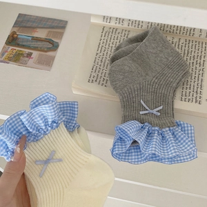 Dettaglio di polsini con volant e fiocchi blu su calze in maglia beige e grigie