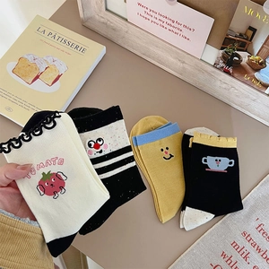 Close-up of four pairs of cotton socks with cartoon embroidery and ruffled edges on a desk