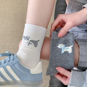 Dettaglio del ricamo a cucciolo e fiocco 3D su calze color crema e grigie