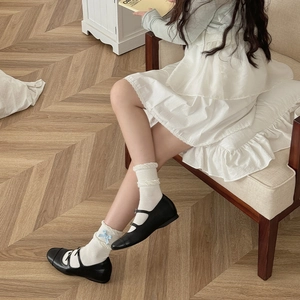 Close-up of white mid-calf socks with lace trim and blue bows with black Mary Jane shoes