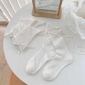 Détail de chaussettes blanches en résille avec cœurs ajourés et nœuds en ruban soyeux