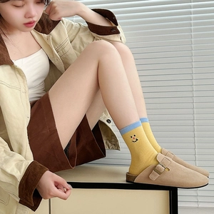 Detail of yellow cotton socks with smiley face embroidery and beige suede mules