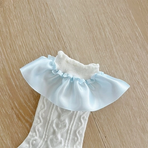 Détail de chaussettes en maille blanche avec dentelle cœur et froufrous en satin bleu