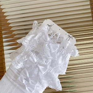 Detail of white lace socks featuring satin bows and intricate hollow-out knit patterns