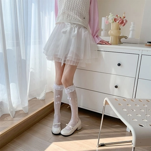 Close-up of white lace cutout knee-high socks with small bows and layered mesh skirt