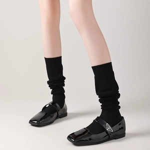 Close-up of black patent leather Mary Jane shoes with matching long knit socks