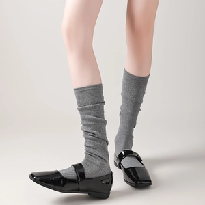 Close-up of grey knitted slouch socks paired with black patent leather Mary Jane shoes