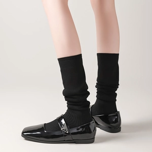 Close-up of black patent leather Mary Jane shoes with metal logo and mid-calf socks