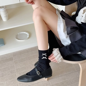 Detail of black rib-knit mid-calf socks with delicate white bow embroidery for a ballet style