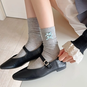 Detail of light gray knit socks with blue ribbon lacing worn with black Mary Jane shoes
