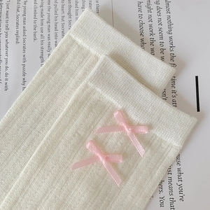 Close-up of cream white ribbed socks featuring sweet pink satin ribbons and bows